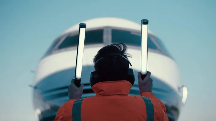 An airport marshal with lighted wands guides a jet