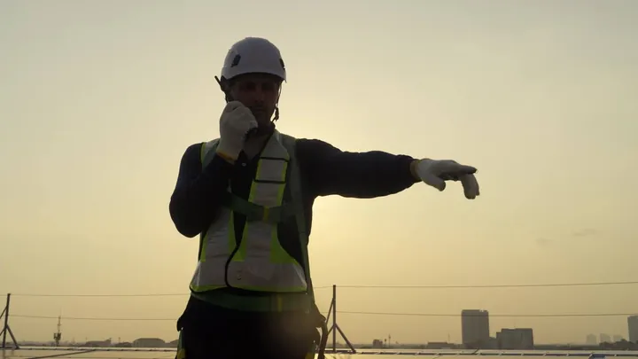 Poster frame from the first hero video: a worker in a hard hat pointing at dusk