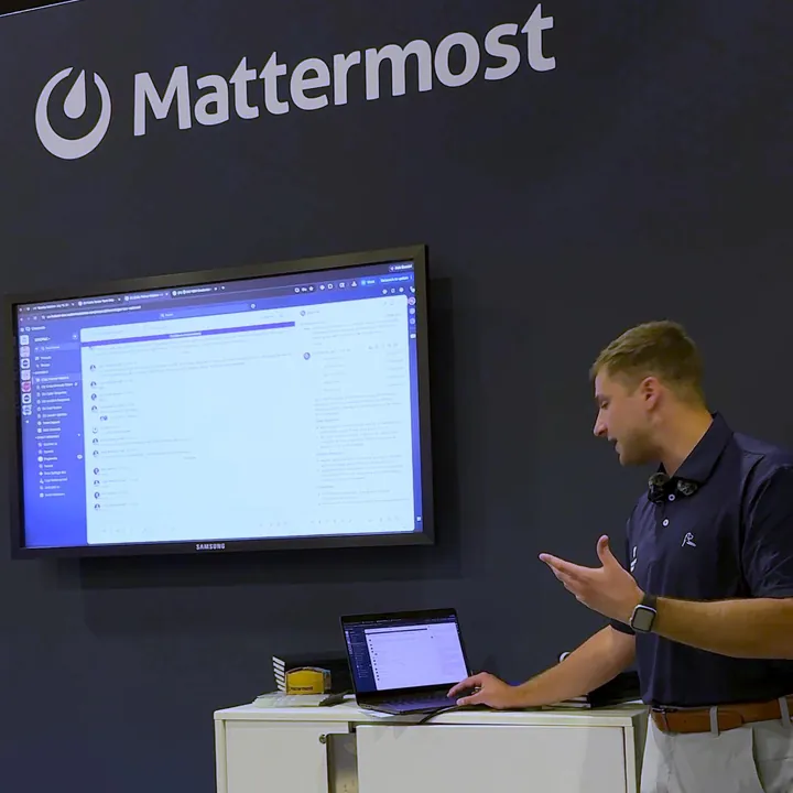 A Mattermost presenter giving a demo at the booth, in front of a large screen and the Mattermost logo