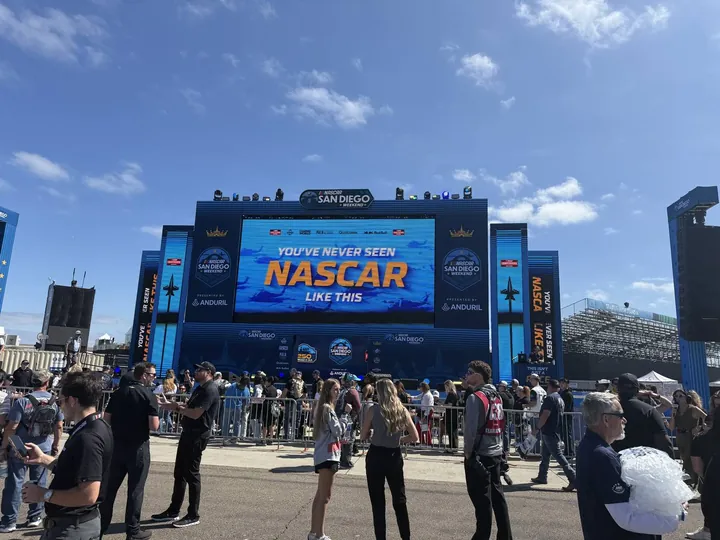 Fans in front of a large NASCAR stage screen