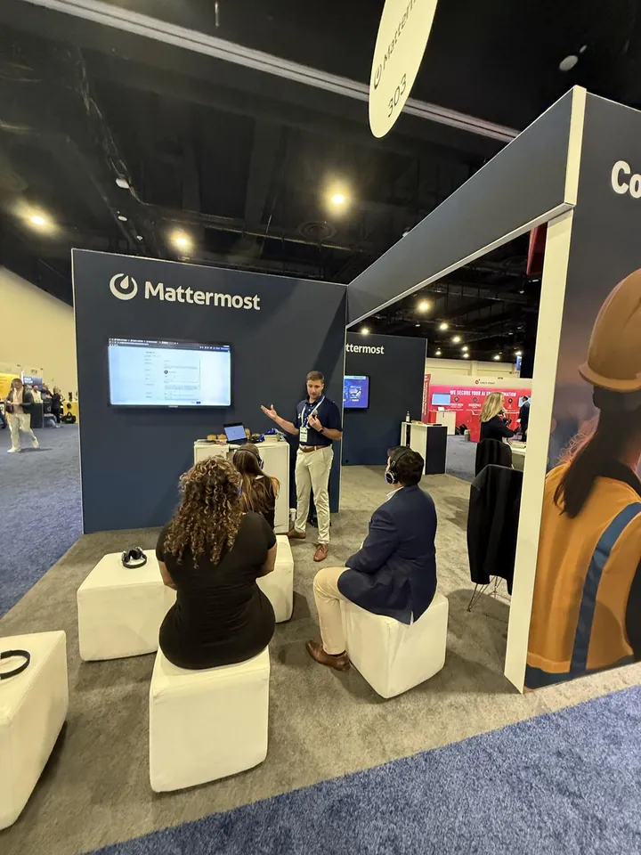 A presenter giving a demo to seated attendees wearing headphones at the Mattermost booth