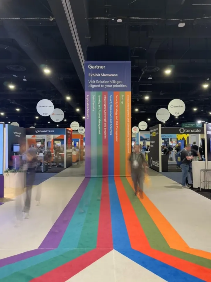 Rainbow carpet stripes leading to a Gartner Exhibit Showcase banner, with attendees blurred in motion
