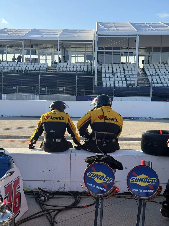 Two pit crew members sit on the pit wall facing the empty grandstand