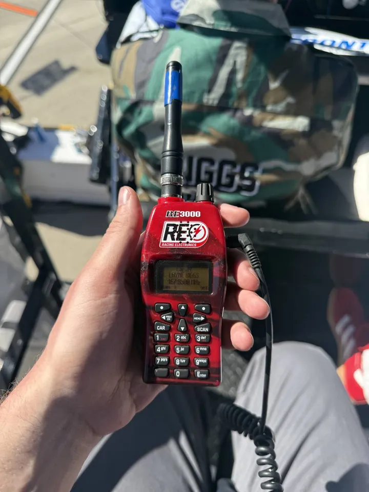 A hand holding a race scanner radio above pit road