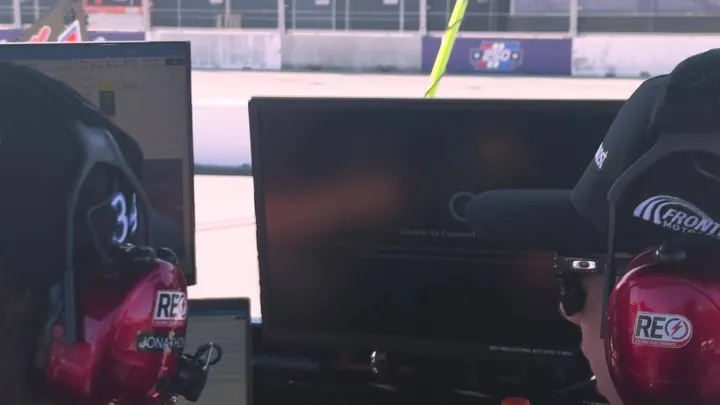 Crew member in a headset in front of pit box monitors