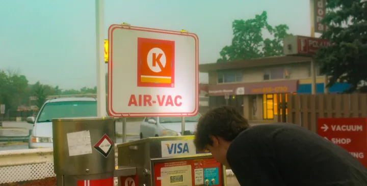 A man at an air and vacuum station under a red sign