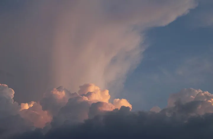A tall storm cloud lit pink at dusk