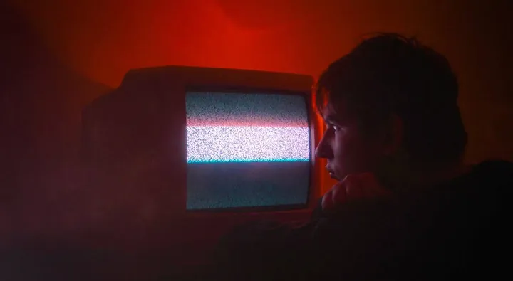 A figure lit red beside a television showing static